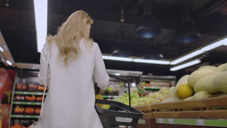 Back-view-Young-housewife-with-basket-shopping-at-the-grocery-store.-Cute-girl-goes-to-the-grocery-department-and-puts-in-the-basket.-Concept-purchase-shop-advertise-buyer-product-bakery