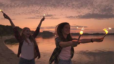 Happy-smiling-girls-running-on-the-beach-with-sparklers-at-night.-Hold-the-sparkling-lights-and-laugh-Carefree-young-students