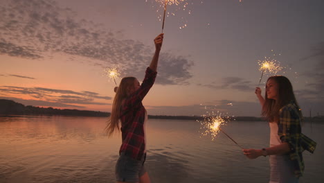 A-group-of-friends-girls-and-men-dance-on-the-beach-with-sparklers-in-slow-motion-at-sunset.-Celebrate-new-year-on-the-beach