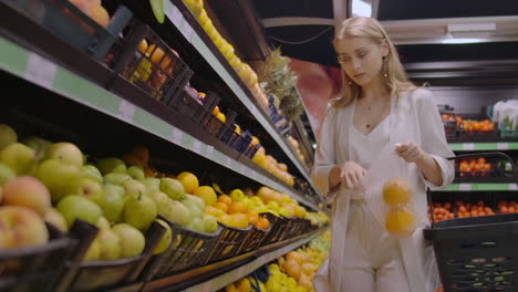 A-beautiful-blonde-in-the-supermarket-chooses-oranges-and-puts-them-in-a-bag-to-weigh-on-the-scales.