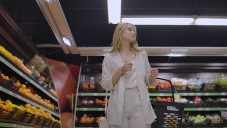 A-beautiful-woman-walks-through-the-supermarket-with-a-basket-in-her-hands-looking-at-the-shelves-of-fruit.-Buying-fresh-fruits-and-vegetables.