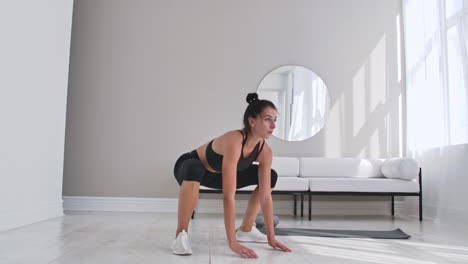 Beautiful-slim-woman-in-thirties-with-fair-complexion-does-morning-strenth-and-aerobic-burpee-exercises-in-modern-airy-room