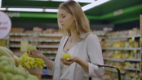 Attractive-young-woman-choosing-apple-at-fruit-vegetable-supermarket-marketplace