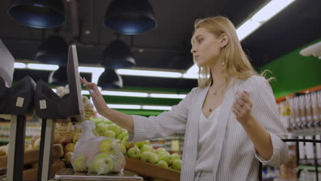 Young-Woman-Weighing-Apples-on-the-Electronic-Scales.-Housewife-Shopping-in-a-Supermarket-in-the-Department-of-Fruit-and-Vegetables.-Slow-Motion.-Sale-Shopping-Consumerism-and-People-Concept