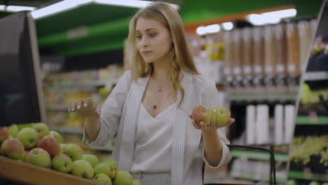 Attractive-young-woman-choosing-apple-at-fruit-vegetable-supermarket-marketplace