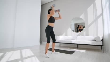 Strong-and-Fit-Beautiful-Girl-in-an-Athletic-Top-is-Doing-Squat-Exercises-in-Her-Bright-and-Spacious-Living-Room-with-Minimalistic-Interior