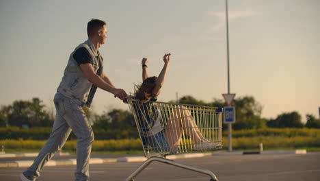 Linseneffekt:-Fröhliches-Paar,-Mann-Und-Frau,-Fährt-Bei-Sonnenuntergang-In-Zeitlupe-Mit-Einkaufswagen-Im-Supermarkt.