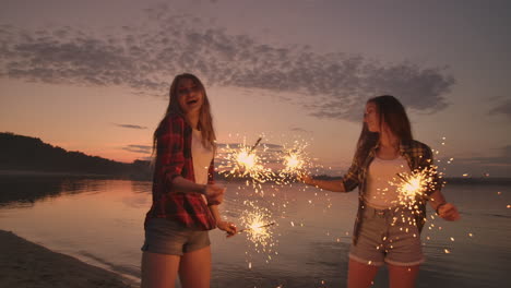 A-group-of-friends-girls-and-men-dance-on-the-beach-with-sparklers-in-slow-motion-at-sunset.-Celebrate-new-year-on-the-beach
