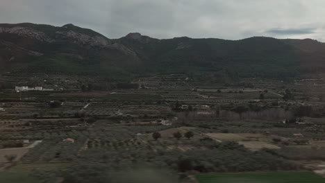 Green-landscape-with-mountains-and-farmland-in-train-window