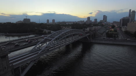 Abendansicht-Einer-Eisenbahnbrücke-Neben-Der-Straßenbrücke-Mit-Einer-Stadtlandschaft-Im-Hintergrund