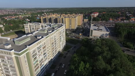 An-aerial-view-of-multi-storey-buildings-next-to-the-green-forest-against-blue-sky