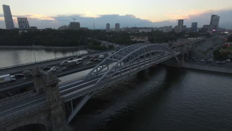 An-aerial-view-of-a-railway-bridge-over-the-river-against-the-evening-urban-view