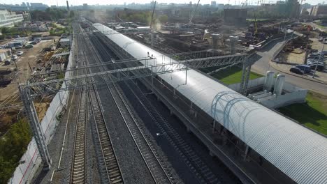 Electric-train-arriving-to-the-station-in-city-outskirts-aerial-view