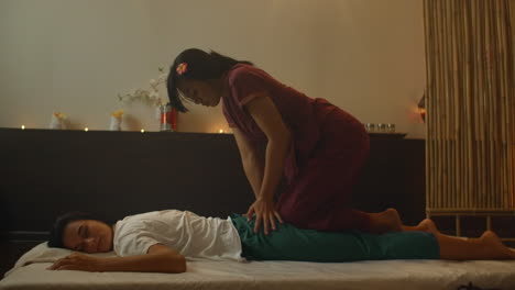 Asiatische-Frau-Führt-Bei-Schöner-Europäischer-Frau-Eine-Traditionelle-Thai-Massage-Durch.-Rehabilitation-Und-Behandlung-Nach-Verletzungen-Mit-Hilfe-Einer-Massage.-Entspannen-Und-Erholen-Sie-Sich-Von-Der-Massage-Der-Beine,-Arme-Und-Des-Rückens.-Therapeutische-Massage