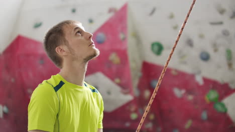 Portrait-of-beautiful-man-rock-climber-belaying-another-climber-with-rope.-Indoors-artificial-climbing-wall-and-equipment.