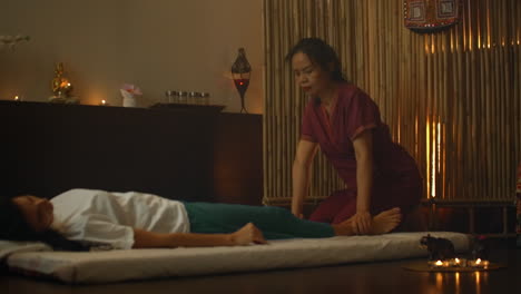 Alternative-Chinesische-Medizin:-Eine-Asiatische-Frau-Führt-Therapeutische-Massagebewegungen-Am-Rücken-Und-Den-Beinen-Einer-Auf-Einer-Couch-Liegenden-Kaukasischen-Frau-Aus.-Traditionelle-Chinesische-Massage.