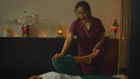 Asian-performs-massage-in-national-clothes-of-Thailand.-Asian-Spa-salon-in-Europe.-Young-Caucasian-woman-relaxes-while-performing-massage.