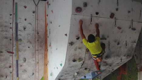 Young-man-Rock-climber-is-Climbing-At-Inside-climbing-Gym.-slim-pretty-man-Exercising-At-Indoor-Climbing-Gym-Wall.