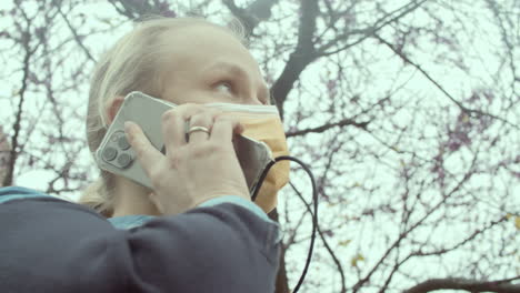 Female-in-mask-speaking-on-smartphone-in-park