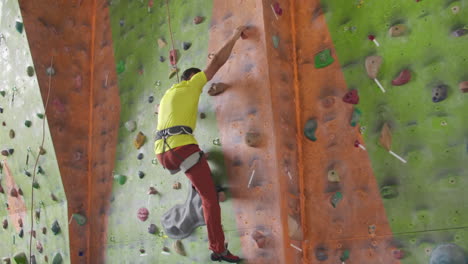 Climber-moves-on-the-mountain-in-a-room-with-a-rope-on-the-insurance-and-a-bag-for-chalk-overcoming-the-height-rises-to-the-top-in-slow-motion