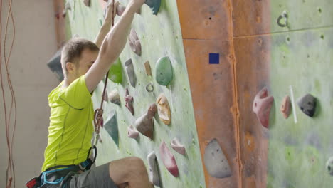 Portrait-of-a-climber-preparing-to-climb-the-wall-in-the-hall-to-chalk-his-hands-and-climb-the-wall-with-insurance-in-slow-motion.