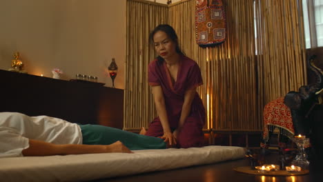 Alternative-Chinesische-Medizin:-Eine-Asiatische-Frau-Führt-Therapeutische-Massagebewegungen-Am-Rücken-Und-Den-Beinen-Einer-Auf-Einer-Couch-Liegenden-Kaukasischen-Frau-Aus.-Traditionelle-Chinesische-Massage.