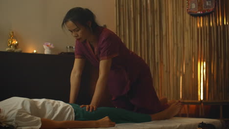 An-Asian-woman-performs-a-traditional-Thai-massage-on-the-back-of-a-lying-beautiful-European-girl.-Chiropractor-produces-treatment-with-alternative-methods.