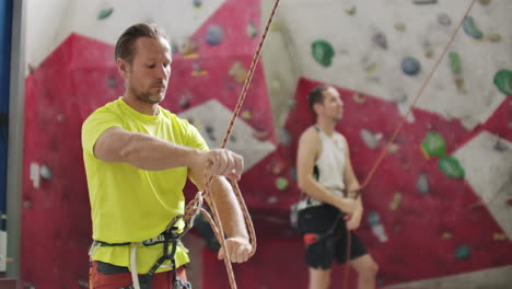 Man-belaying-another-climber-on-an-indoor-climbing-wall.-A-man-using-insurance-climbers-holds-the-rope-and-insures-his-partner-who-climbs-the-mountain