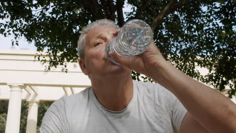 A-sporty-elderly-caucasian-man-drinks-water-after-fitness-classes