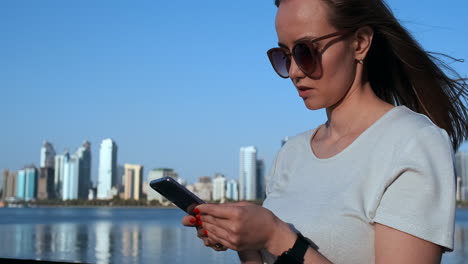 A-girl-with-long-hair-dials-a-message-on-the-smartphone-at-the-quay-of-Dubai