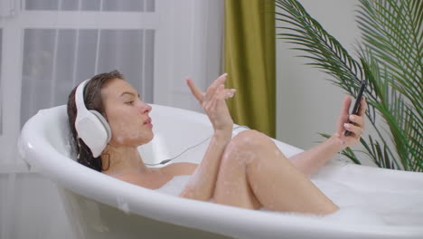 Hermosa-Mujer-Escuchando-Música-En-La-Bañera-Disfrutando-De-Un-Relajante-Estilo-De-Vida-De-Baño-De-Burbujas,-Cuidado-Corporal-Natural-Real
