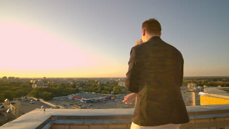 A-man-and-a-woman-standing-on-the-roof-at-sunset-embrace-and-look-at-the-beautiful-view.