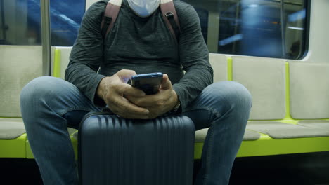 Man-traveler-with-suitcase-using-phone-in-subway-train