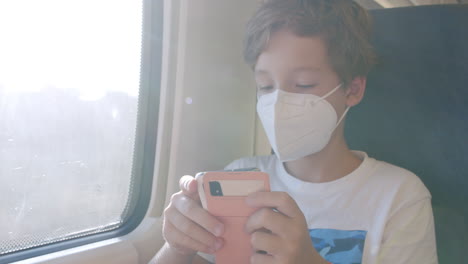 Boy-in-mask-traveling-by-train-and-using-phone