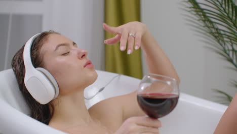 Just-relax.-Content-beautiful-young-woman-listening-to-music-and-closing-her-eyes-while-taking-a-bath.