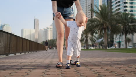Young-mother-with-a-child-and-first-steps.-Young-mother-with-a-child-at-outdoor-learninig-for-a-first-steps-near-urban-in-the-city