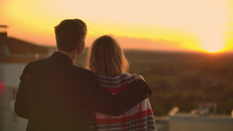 Lovers-embracing-guy-girl-watching-the-sunset-with-wine-standing-on-the-roof-of-the-building.-Slow-motion-picture-of-the-relationship-of-a-married-young-couple.