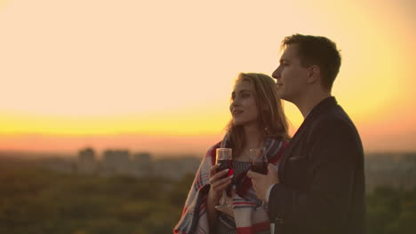 Lovers-embracing-guy-girl-watching-the-sunset-with-wine-standing-on-the-roof-of-the-building.-Slow-motion-picture-of-the-relationship-of-a-married-young-couple.