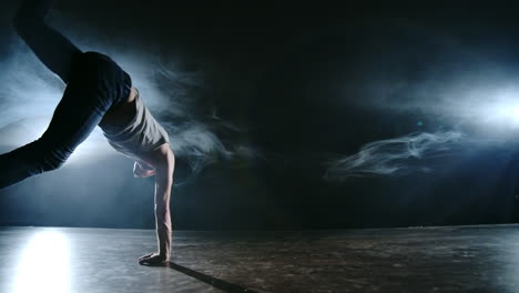 Male-dancer-performs-a-stunt-jump-with-a-rotation-back-and-a-revolution-in-the-scene-in-the-smoke-in-the-spotlight.-Modern-ballet