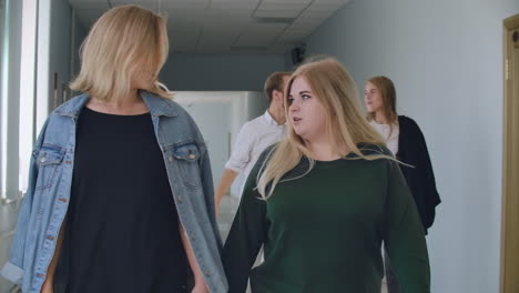 Two-female-students-walk-down-the-hall-of-the-University-and-talk-and-discuss-and-talk.
