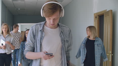 A-young-man-in-headphones-walks-along-the-inversion-corridor-listens-to-music-and-does-not-pay-attention-to-people.-It-is-in-its-own-world.-An-introvert-walks-through-the-college-hall-without-talking-to-students-and-listens-to-music-and-writes-chat-messages