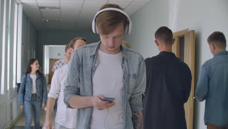 A-man-wearing-headphones-among-the-crowd-of-students-listening-to-music-is-on-the-corridor-of-the-University-during-a-break-between-classes.-An-introvert-in-University-inner-peace.