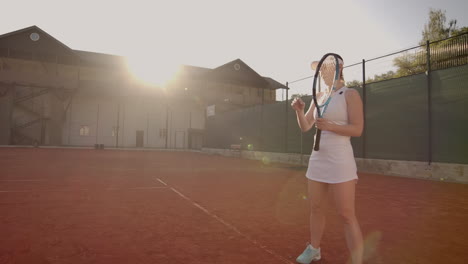 Cheerful-athlete-waiting-for-tennis-ball.-Skillful-female-tennis-player-is-preparing-to-beat-a-ball.-She-is-holding-a-racket-and-posing.-Woman-is-standing-on-tennis