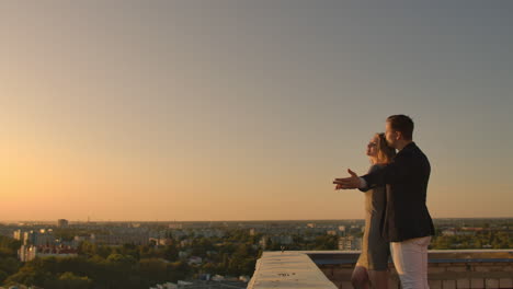 Young-couple-in-love-standing-on-the-roof-hug-and-closely-look-at-each-other.-Romantic-evening-on-the-roof-of-the-building.-A-date-on-the-roof-of-a-building-love.-Slow-motion