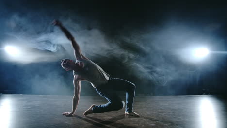 Male-dancer-performs-a-stunt-jump-with-a-rotation-back-and-a-revolution-in-the-scene-in-the-smoke-in-the-spotlight.-Modern-ballet