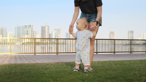 Smiling-Boy-holding-his-mother's-hand-makes-the-first-steps-walking-along-the-promenade-in-the-summer.