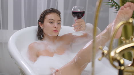 Relax-lying-in-a-white-bath-with-a-glass-of-red-wine.-Young-woman-relaxing-in-hot-relaxing-bath.