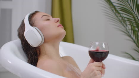 Just-relax.-Content-beautiful-young-woman-listening-to-music-and-closing-her-eyes-while-taking-a-bath.