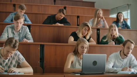 Eine-Große-Gruppe-Multiethnischer-Studenten-Arbeitet-An-Ihren-Laptops,-Während-Sie-Im-Modernen-Klassenzimmer-Einer-Vorlesung-Lauschen.-Kluge-Junge-Leute-Studieren-An-Der-Universität.
