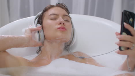 Sexy-Caucasian-brunette-in-headphones-lies-in-a-bubble-bath-and-dances-listening-to-music-in-headphones.